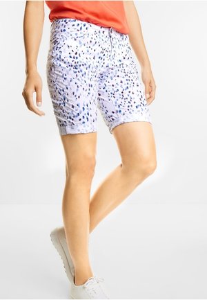 Shorts blancs avec des taches multicolores en bleu et violet. Coupe mi-haute avec des ourlets roulés. Portés avec un haut rouge et des baskets blanches.