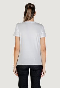 T-shirt bianco a maniche corte con risvolti, design semplice, scollatura rotonda e una texture morbida. Indossato con jeans scuri. Vista laterale.