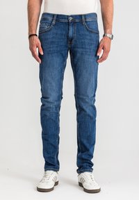 Dopasowane ciemnoniebieskie jeansy z dżinsu o klasycznym kroju z pięcioma kieszeniami, subtelnymi detalami przeszyć i delikatnym blaknięciem, połączone z białymi trampkami.