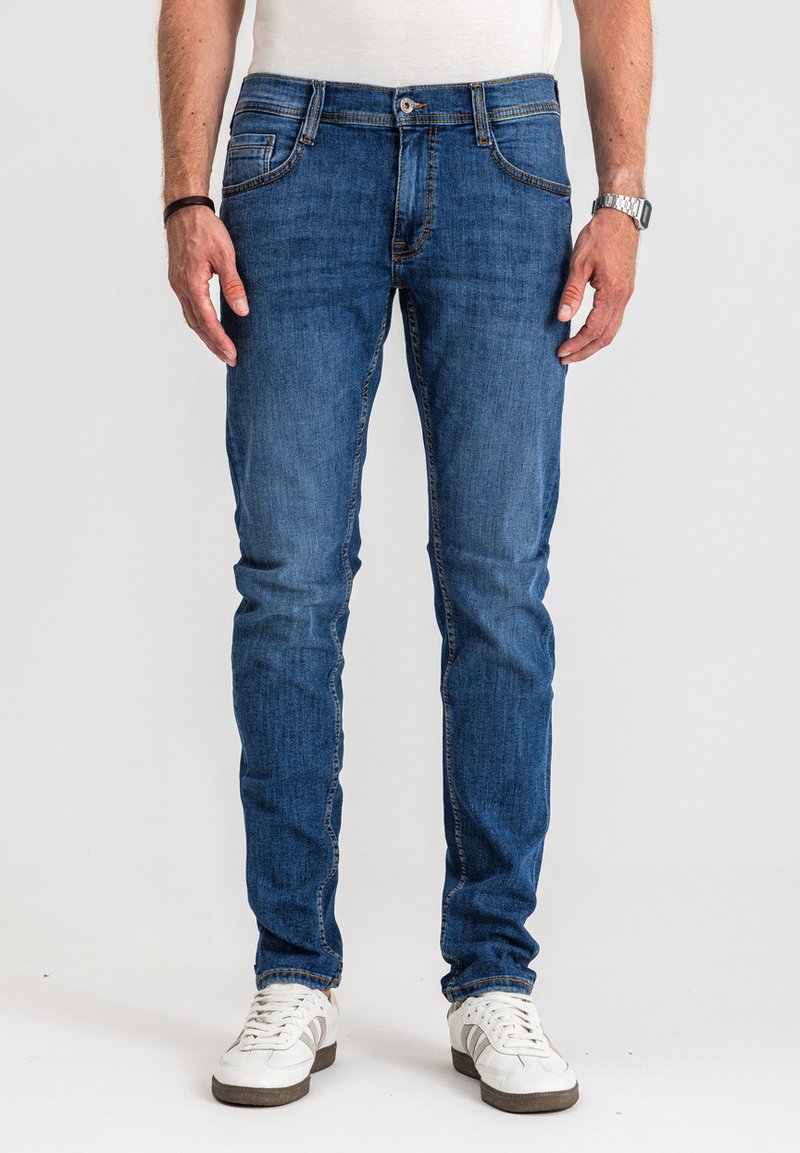 Dopasowane ciemnoniebieskie jeansy z dżinsu o klasycznym kroju z pięcioma kieszeniami, subtelnymi detalami przeszyć i delikatnym blaknięciem, połączone z białymi trampkami.