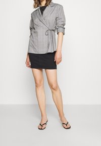 Grijze geruite wikkeljas met lange mouwen, strik taille-detail, gecombineerd met een zwarte denim mini-rok en zwarte flip-flops.