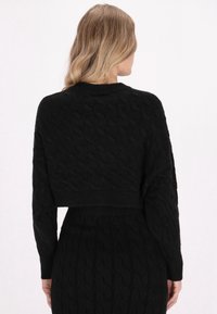 Schwarzer gestrickter Cropped-Pullover mit strukturiertem Kabelmuster und langen Ärmeln. Weicher Stoff mit geripptem Saumdetail, kombiniert mit einem passenden Rock.