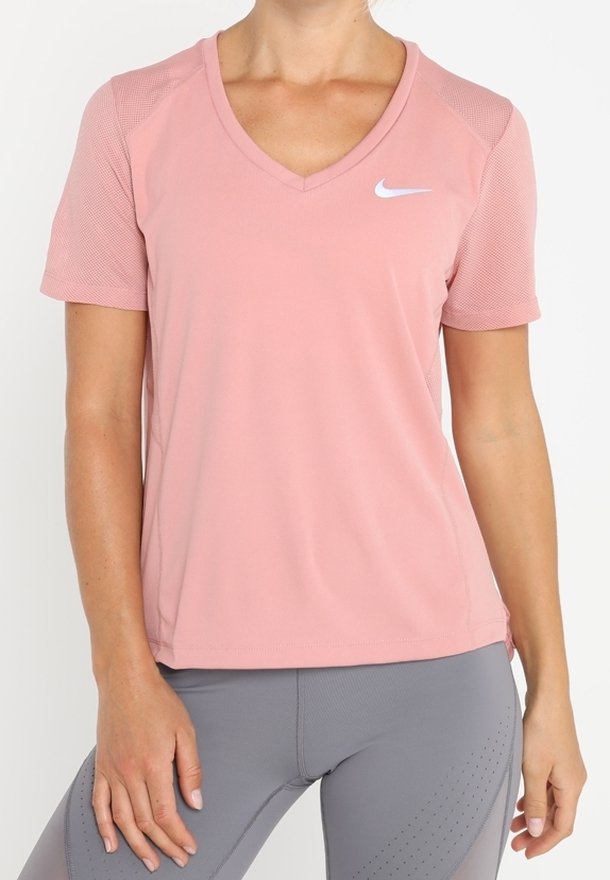 Femme portant un t-shirt de sport à manches courtes rose Nike avec un col en V et un legging de sport gris avec des détails perforés subtils.