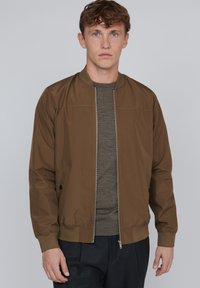 Brown bomber jacket with a zip front, ribbed cuffs, and side pockets. Smooth fabric texture, casual design, suitable for layered outfits.