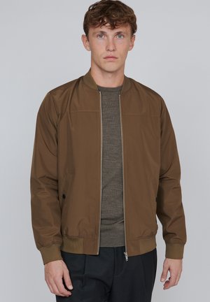 Veste bomber marron avec fermeture éclair à l'avant, poignets côtelés et poches latérales. Texture de tissu lisse, design décontracté, adapté aux tenues superposées.