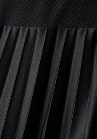 Tissu plissé noir avec une section supérieure texturée. Les plis sont uniformes et finement détaillés, mettant en valeur une surface lisse avec un éclat subtil.