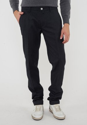 Pantaloni grigi scuri realizzati in un tessuto testurizzato, con chiusura a bottone, tasche inclinate e una vestibilità comoda, abbinati a sneakers bianche.