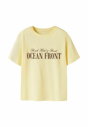 Light yellow short-sleeve T-shirt with round neck, featuring brown text "Beach Hotel & Resort OCEAN FRONT" on front center.