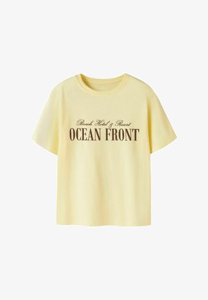 Lysegul T-shirt med korte ærmer og rund hals, med brun tekst "Beach Hotel & Resort OCEAN FRONT" midt foran.