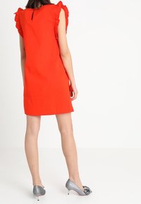 Czerwona krótka sukienka z falbaniastymi rękawami i dekoltem w kształcie łezki, połączona z błyszczącymi srebrnymi szpilkami z ozdobami w postaci kokardek.