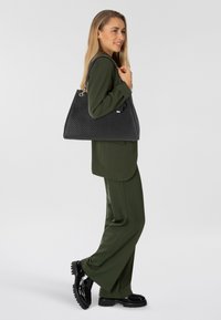 Borsa hobo nera trapuntata con finitura testurizzata, dotata di hardware argentato e doppi manici, tenuta con nonchalance da una persona in un completo verde.