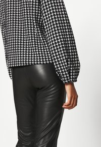 Blouse à motif pied-de-poule noir et blanc avec des manches bouffantes, associée à un pantalon en cuir noir ajusté. Texture lisse et coupe taillée.
