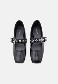 Μαύρα παπούτσια με τετράγωνη μύτη και γυαλιστερό φινίρισμα, με λουράκι με αγκράφα διακοσμημένο με ασημένια μεταλλικά τρουκ. Λείο δέρμα.