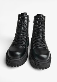 Czarne skórzane buty trekkingowe z masywną, teksturowaną gumową podeszwą, metalowymi elementami i skomplikowanym systemem sznurowania. Zamek błyskawiczny po boku.