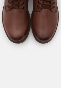 Calzado de cuero marrón con un acabado suave, punta redonda y diseño tradicional con cordones. Presenta costuras reforzadas y suela texturizada.