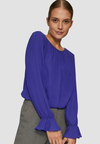 Paarse blouse met geplooide lange mouwen en een ronde halslijn. De mouwen hebben gerimpelde manchetten. Gemaakt van gladde, lichte stof.