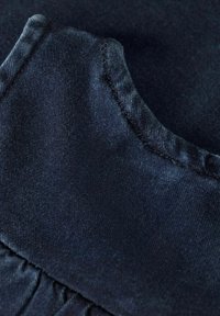 Tamsiai mėlyna medžiaga su švelniu paviršiumi, turinti raukšlėtą apykaklės detalę ir kontrastingą siuvinėjimą kraštuose.