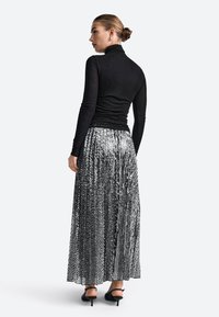 Juodas golfo megztinis, derinamas su klostuota, blizgančia sidabrine paillettes maksi sijonu. Sijonas turi vertikalias linijas ir plazdančią struktūrą.