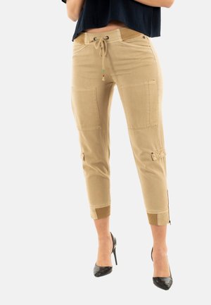 Pantaloni cargo tagliati beige con vita elasticizzata, coulisse, due grandi tasche frontali e polsini a coste. Abbinati a tacchi alti neri.