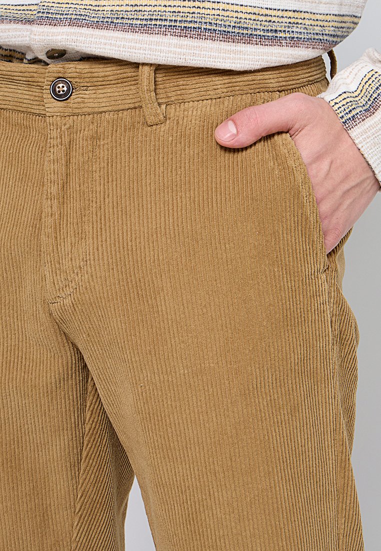 Pantaloni in corduroy marrone con texture a righe verticali, dotati di chiusura con bottone e tasca laterale. Cuciture più chiare lungo le cuciture.