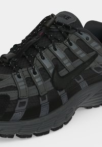 Μαύρο και σκούρο γκρι αθλητικό παπούτσι Nike με ανακλαστικές ρίγες, ελαστικά κορδόνια με κλείδωμα και ορατή λεπτομέρεια μαλακής σόλας.