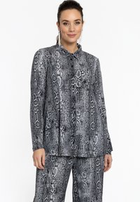 Blouse à imprimé serpent noir et gris avec un col, dotée de boutons sur le devant et de manches longues. Tissu lisse avec une coupe ajustée.