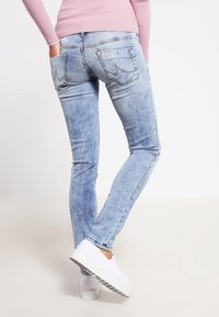 Vaaleansiniset farkut, joissa on kapea malli ja hienoinen haalistuminen, takana kaksi taskua koristeompeleilla, yhdistettynä valkoisiin liukusuojuksiin.