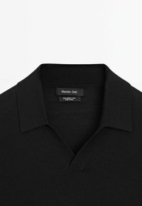 Sort merinould polo sweater med V-hals og kort krave. Har en glat tekstur, minimal design og et diskret mærke.