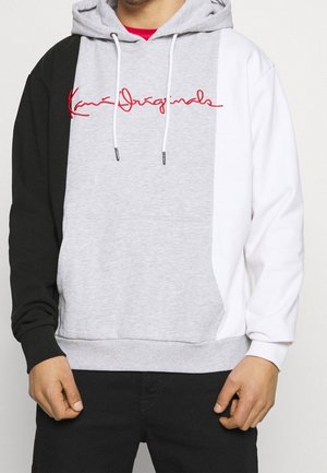 Mand iført en color-block hoodie med sort ærme, grå midte, hvidt ærme og rød script-logo tværs over brystet.