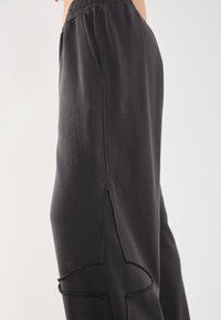 Black sweatpants made of soft material, featuring angled side pockets and visible stitching details along the seams. Elastic waistband.