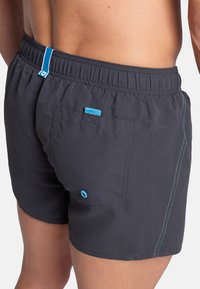 Pantaloni da bagno da uomo in tessuto grigio scuro con vita elasticizzata. Presentano un cordino blu a contrasto e una tasca con un accento blu.