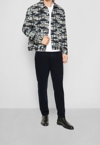 Flerfärgad mönstrad jacka med svart, vit och blå design, matchad med mörka byxor och svarta ankelstövlar. Slät textur, knappstängning.