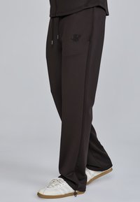 Black, tapered sweatpants with an elastic waistband and drawstring; featuring logo detail and zip openings at the ankles. Paired with white sneakers.
