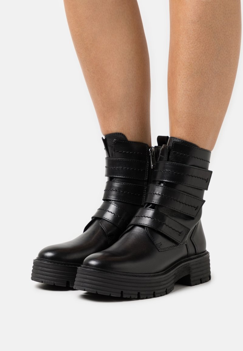 Bottines noires en cuir avec plusieurs sangles horizontales, un bout arrondi, une semelle épaisse et une fermeture éclair sur le côté pour un enfilage facile.
