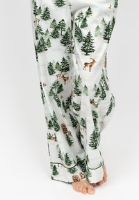 Pantalones de pijama blancos con un patrón de bosque que incluye árboles verdes, ciervos y osos. Corte holgado, tejido ligero. Textura suave.