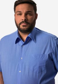 Camicia a maniche corte blu con bottoni in tessuto texturizzato, colletto e taschino sul lato sinistro. Presenta bottoni blu e una vestibilità comoda.