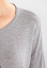 Szary sweter z okrągłym dekoltem, wykonany z miękkiej, teksturowanej tkaniny. Rękawy mają luźny krój z delikatnym drapowaniem.