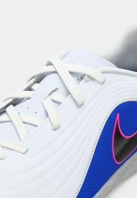 Λευκό αθλητικό παπούτσι με λευκές κορδόνες και μπλε πλευρική πάνελ που διαθέτει ένα λογότυπο σε σχήμα σούσουρα σε μαύρο και ροζ περίγραμμα.