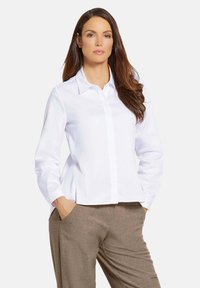 Witte langydym shirt met een spitse kraag, knopen aan de voorkant en een relaxte fit, gecombineerd met bruine broeken van een textuurstof.
