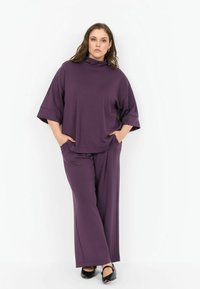 Set de lounge purpuriu, compus dintr-o bluză lejeră cu guler înalt și mâneci lărgi, asociată cu pantaloni cu picioare largi. Material moale, design minimalist.