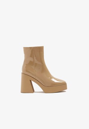 Bottines en cuir verni beige avec un embout carré, un talon bloc haut et une semelle à plateforme, présentant une finition lisse et brillante.