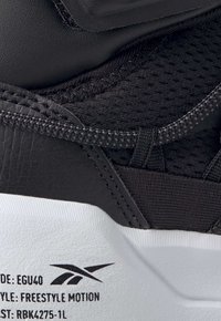 Svart sneakers med överdel i läder och mesh, texturerad yta, vadderat ankelsupport och vit gummisula med modellinformation på sidan.