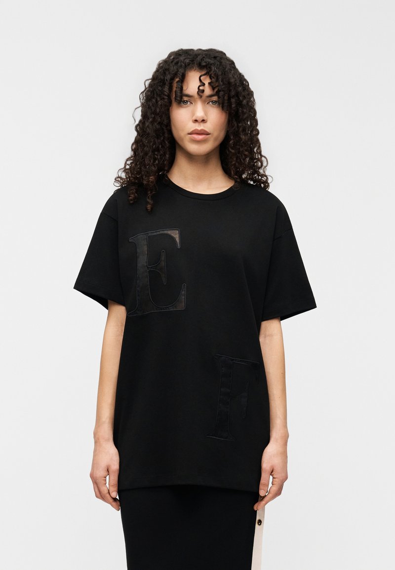Μαύρο βαμβακερό T-shirt με μεγάλα μαύρα υφασμάτινα γράμματα "E" και "F" στο μπροστινό μέρος, με κοντά μανίκια και άνετη εφαρμογή.