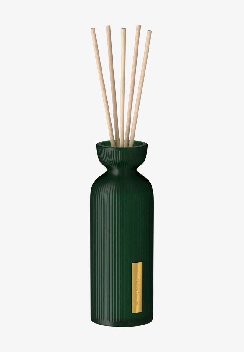 Diffuseur en verre vert cannelé avec un col évasé, comportant cinq tiges en bois naturel et une petite étiquette dorée à l'avant.