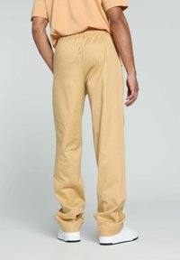 Helle beige Baumwollhose mit elastischem Bund, gerade Beinform und glatter Textur, kombiniert mit weißen Sneakers, von hinten gesehen.