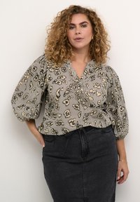Graue Bluse mit einem Leopardenmuster, ausgestattet mit Puffärmeln und einem V-Ausschnitt, kombiniert mit einem schwarzen Jeansrock. Strukturiertes Material.