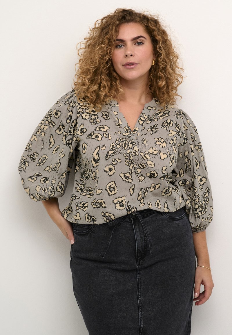 Graue Bluse mit einem Leopardenmuster, ausgestattet mit Puffärmeln und einem V-Ausschnitt, kombiniert mit einem schwarzen Jeansrock. Strukturiertes Material.