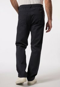 Ciemnoniebieskie, casualowe spodnie z elastycznym pasem, dwiema tylnymi kieszeniami, gładką fakturą materiału i luźnym krojem, w połączeniu z jasnymi butami.