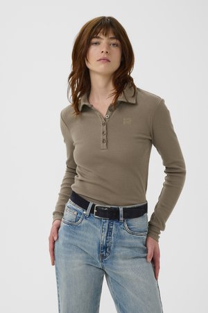 Braunes Poloshirt mit langen Ärmeln und geripptem Stoff, ausgestattet mit Kragen und Knopfleiste; kombiniert mit hellblauen Jeans und einem schwarzen Gürtel.