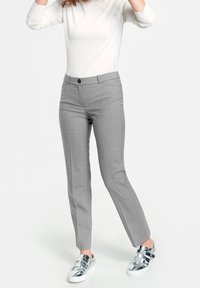 Pantalon gris sur mesure à texture lisse, jambes droites, fermeture à boutons sur le devant, porté avec des baskets argentées brillantes et un haut blanc.
